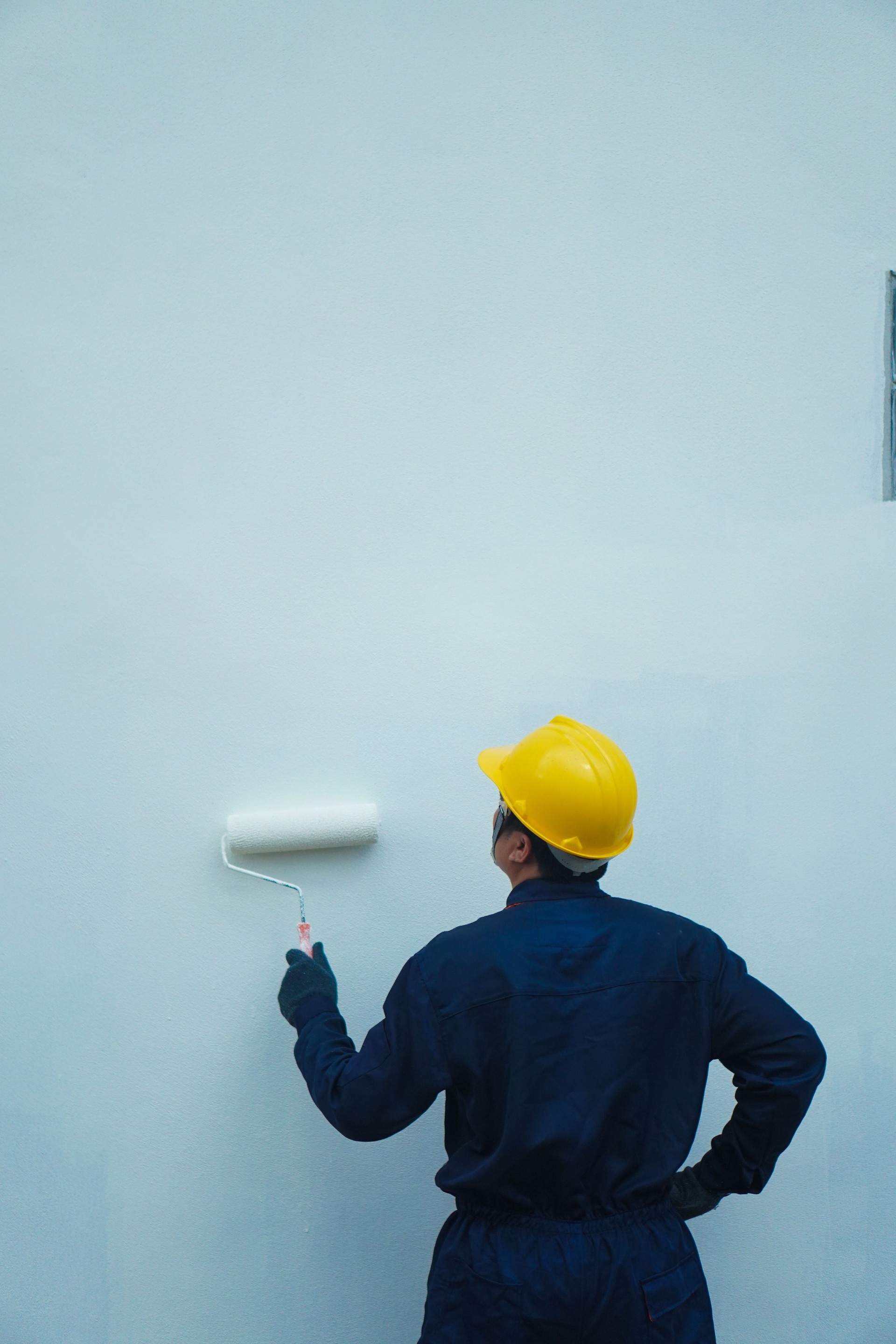 Behind the painter is painting a house wall with a roller, there is space for text.